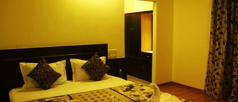 A hotel room with a bed, pillows, a nightstand, a mirror, and a curtain.