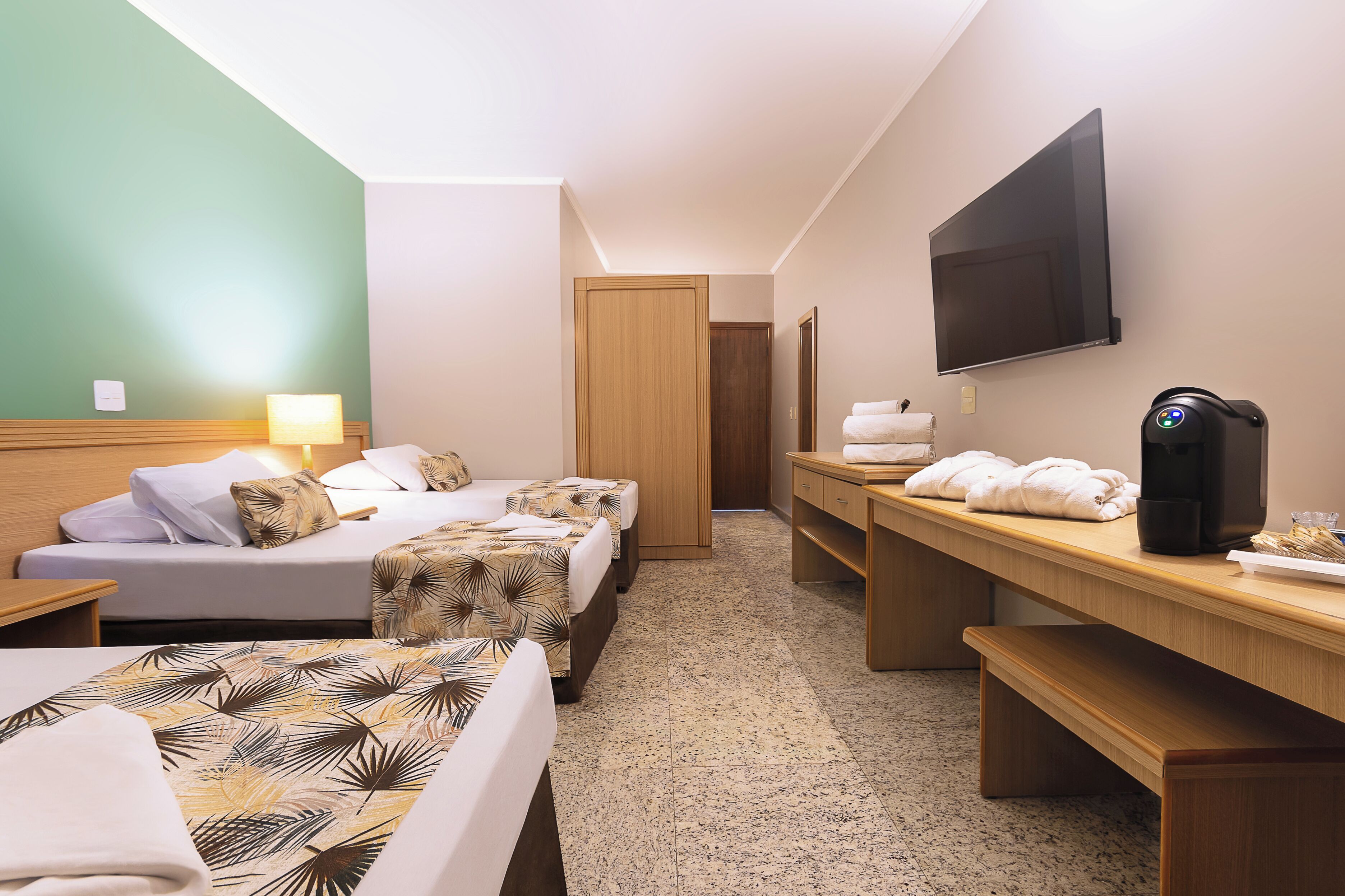 Quarto de hotel com duas camas, uma escrivaninha, televisão, máquina de café e porta de banheiro.