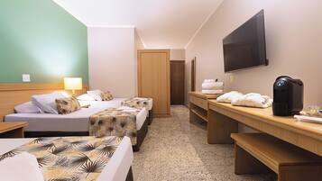 Quarto de hotel com duas camas, uma escrivaninha, televisão, máquina de café e porta de banheiro.