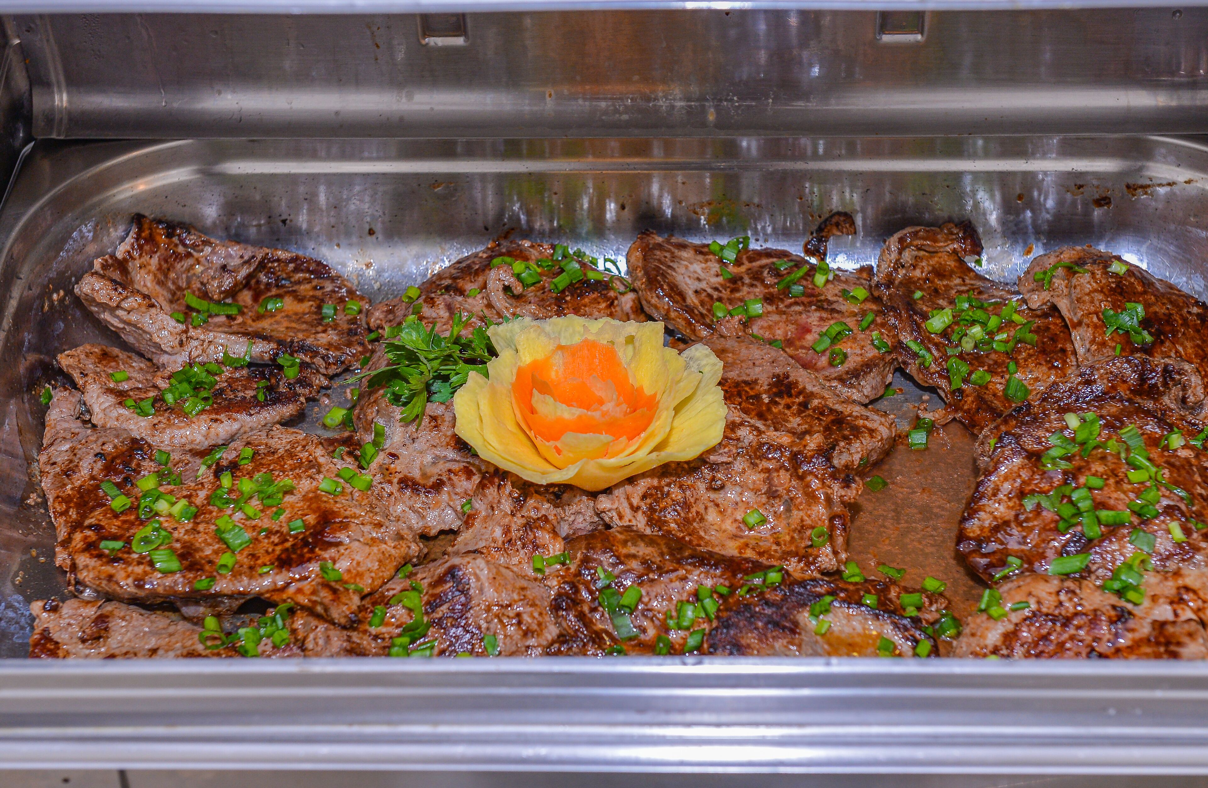 Uma bandeja de carne grelhada decorada com cebolinha picada e uma flor amarela ornamental.