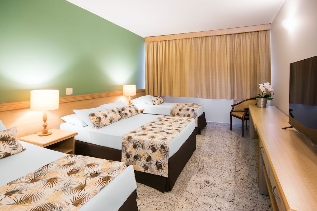 A hotel room with three beds, a desk, and a TV.