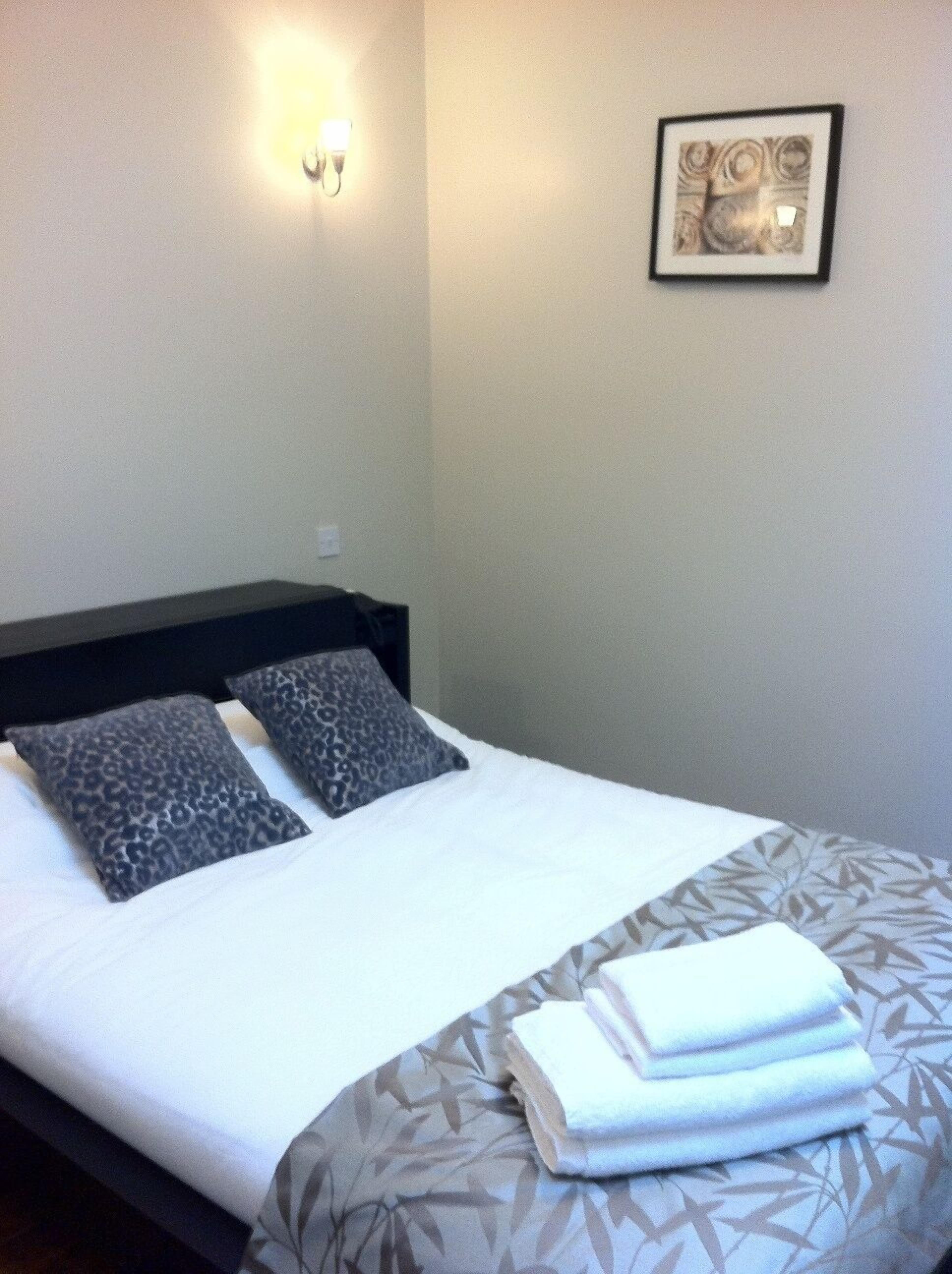 Un lit bien fait, recouvert d’une couvre-lit à motifs et agrémenté de deux coussins à imprimé léopard. Un tableau encadré est accroché au mur, au-dessus du lit.