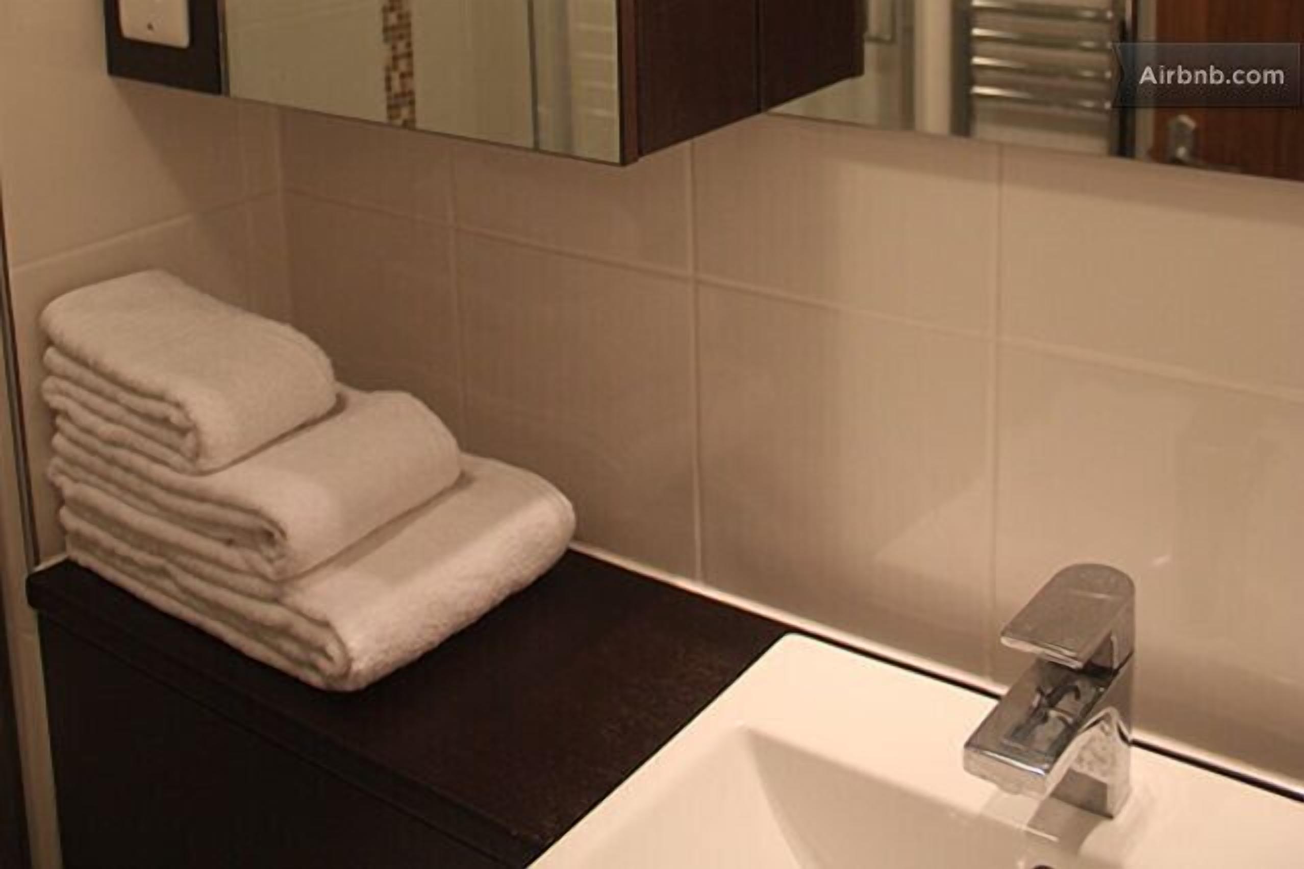 A bathroom with a white sink, a towel stack, and a mirror above the sink.