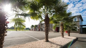 A parking area with palm trees and a building with a modern design. - Brit Hotel Essentiel Pau Lescar (Lescar)