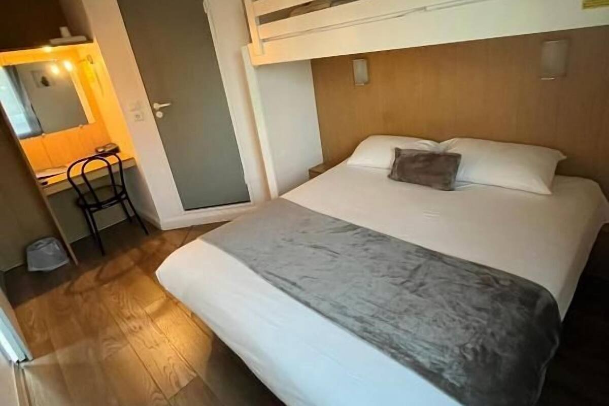 Ein Schlafzimmer mit Etagenbett, Holzboden, Schreibtisch mit Stuhl und einer kleinen Küchenzeile.