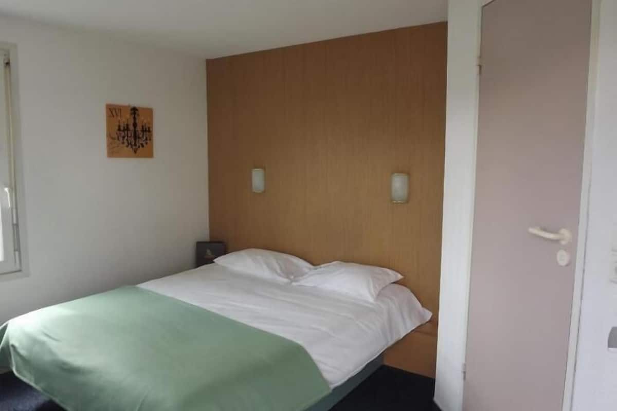 Ein Einzelbett mit einer grün-weißen Tagesdecke, einem Holz-Kopfende, zwei Wandleuchten und einer Tür mit Griff.