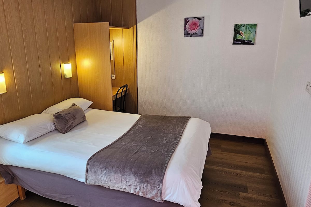 Ein ordentlich bezogenes Bett mit Kissen und Decke, ein Holzschrank und zwei Wandleuchten.
