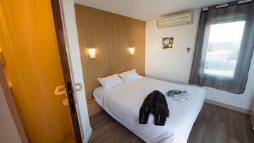 A hotel room with a wooden headboard, a bed with white linens, a jacket on the bed, and a window with curtains.