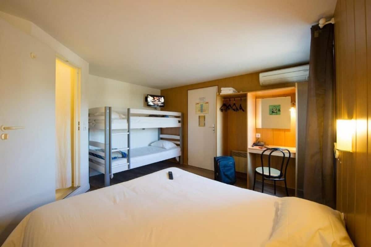Ein Hotelzimmer mit Etagenbett, Schreibtisch, Stuhl, Fernseher und Kleiderschrank.