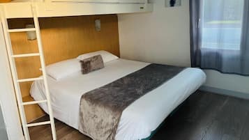 A bunk bed room with a ladder, a wooden headboard, a bedside table, and a window with a sheer curtain.
