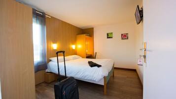 Habitación de hotel con cama, maleta, mesita de noche, televisor de pared y una ventana pequeña.