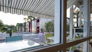 A view of a hotel with outdoor seating and palm trees. - Brit Hotel Essentiel Pau Lescar (Lescar)