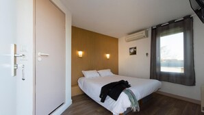 A bedroom with a bed, wooden panel wall, two wall-mounted lights, an air conditioner, and a window with curtains. - Brit Hotel Essentiel Pau Lescar (Lescar)