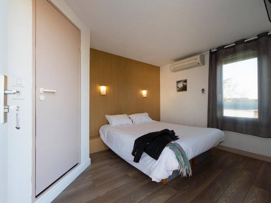 Ein Schlafzimmer mit einem Bett, einer Wandpaneelausstattung, zwei Wandleuchten, einer Klimaanlage und einem Fenster mit Vorhängen.