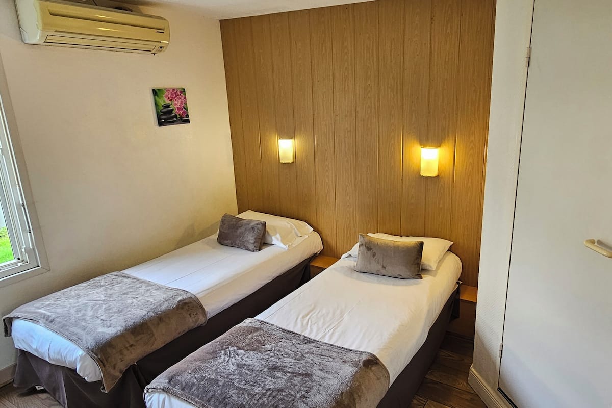 Ein Hotelzimmer mit zwei Einzelbetten, Holzvertäfelung an der Wand, zwei Wandleuchten sowie einer Tür mit Griff und Schloss.