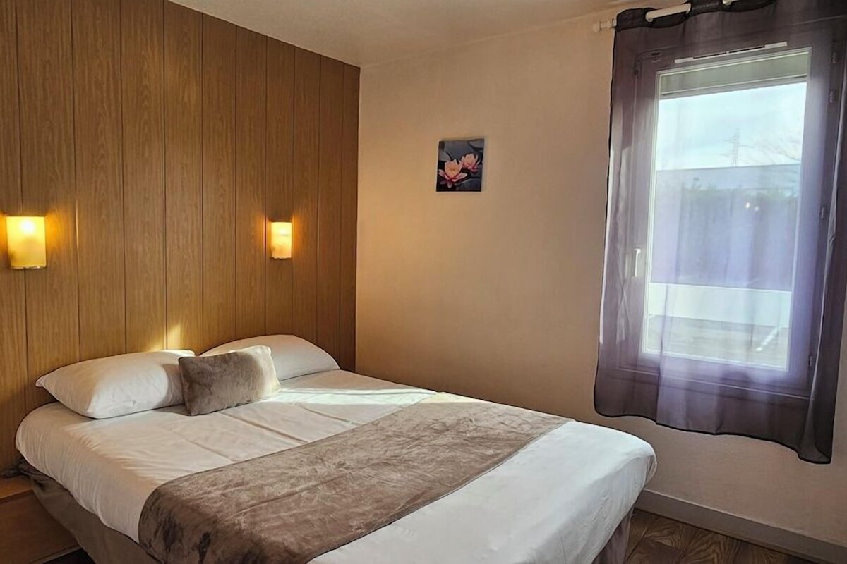 Una cama individual con cabecera de madera, dos lámparas de pared, una ventana con cortina y un cuadro pequeño en la pared.
