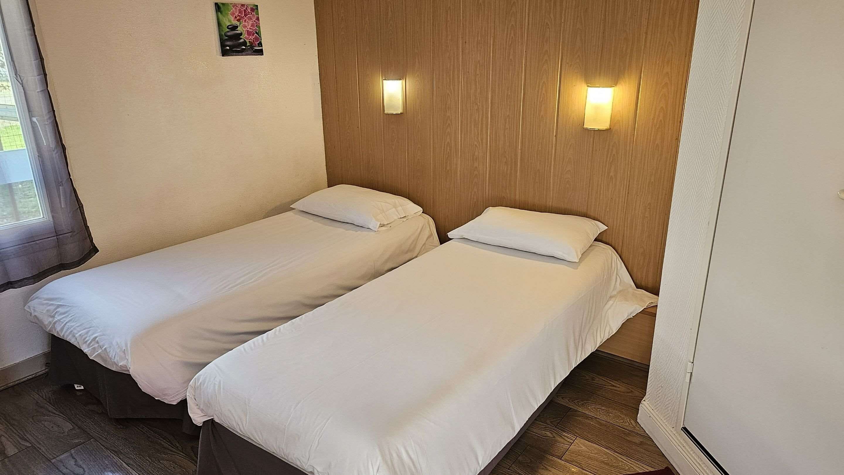 Een kamer met twee eenpersoonsbedden, houten lambrisering en twee wandlampen.
