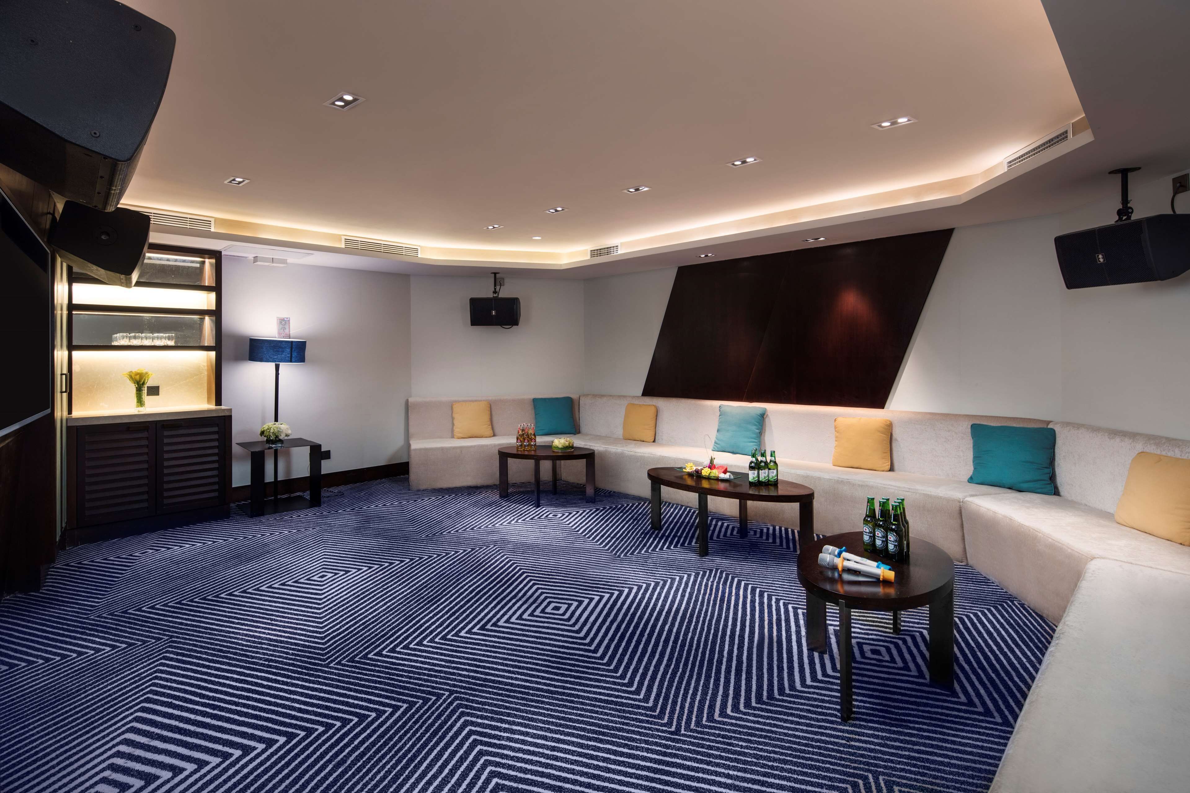 Un espacio lounge moderno con un sofá, dos mesitas y una pared con una pantalla grande.