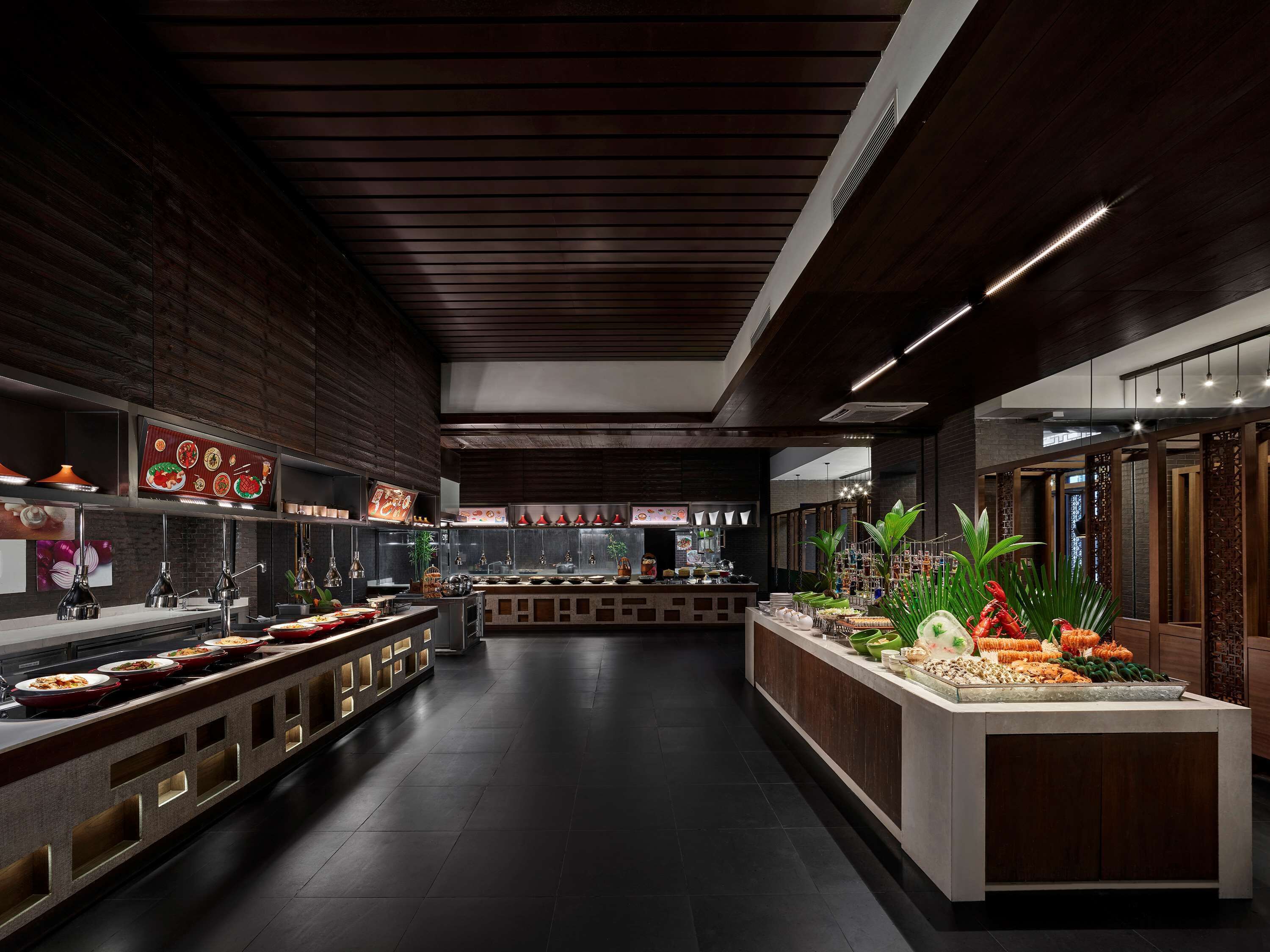 A modern restaurant with a long counter, dark wood paneling, and a variety of dishes displayed.