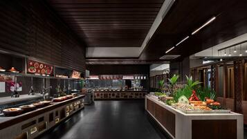 A modern restaurant with a long counter, dark wood paneling, and a variety of dishes displayed.
