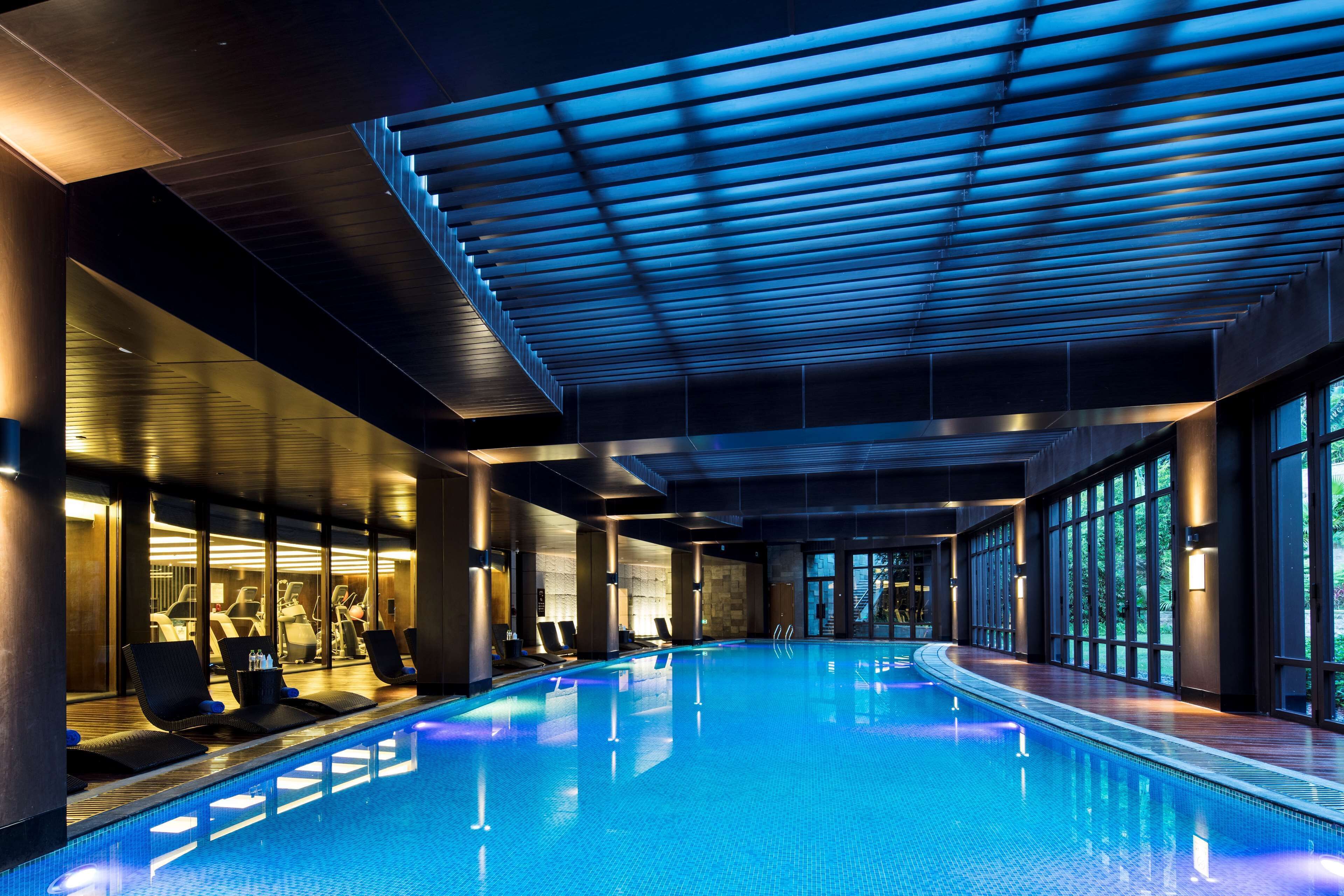 Ein modernes Hallenbad mit blauer Beleuchtung, Liegestühlen und Fitnessgeräten.