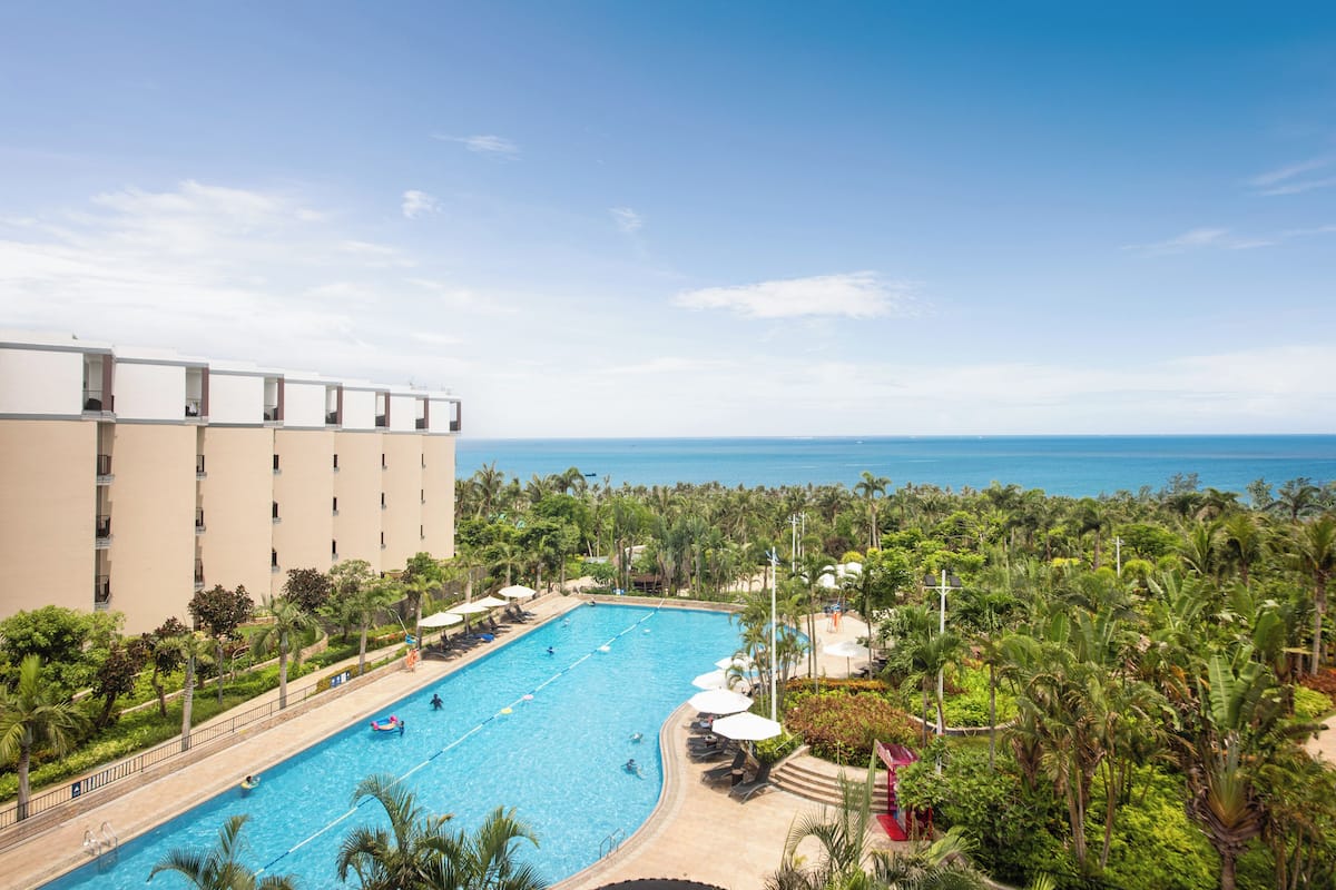 A hotel with a swimming pool surrounded by lush greenery and a view of the ocean.