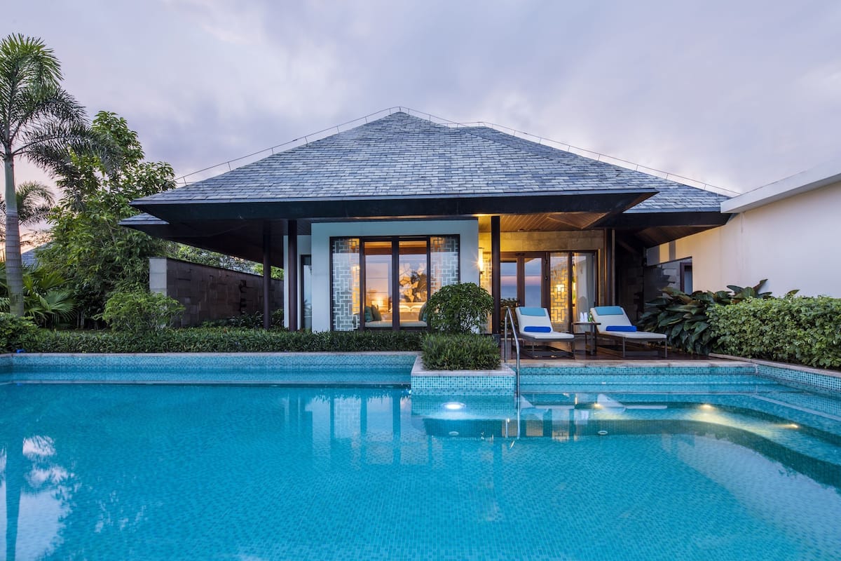 A modern house with a swimming pool, a covered patio with lounge chairs, and a view of the sunset.