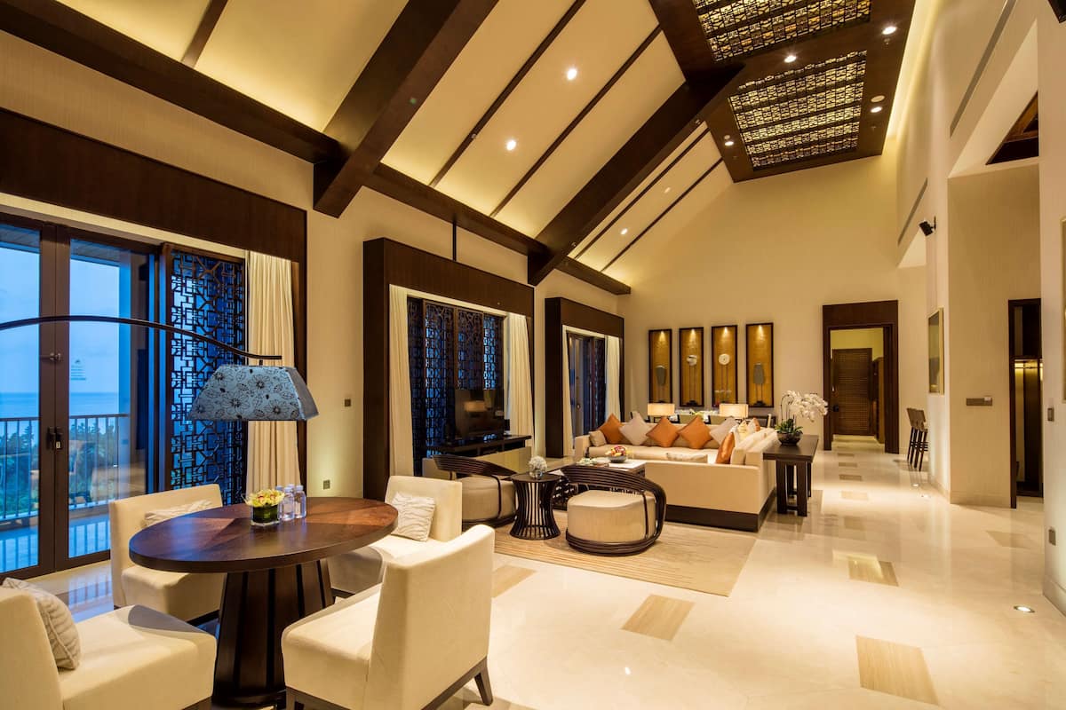 A spacious living room with a large sofa, a coffee table, and a TV. There is a balcony with a view of the ocean.