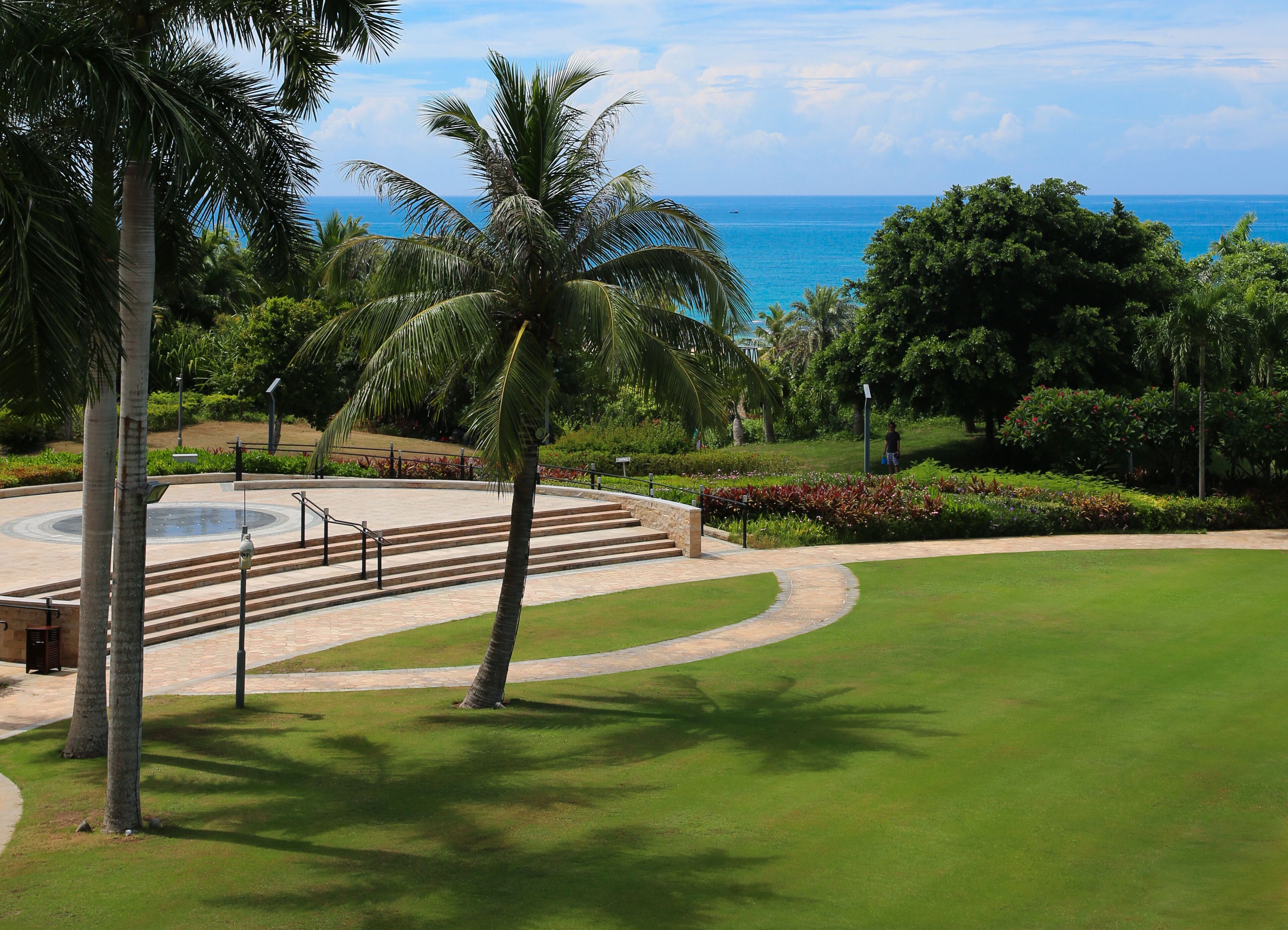 A landscaped area with a circular water feature, palm trees, and a view of the ocean.