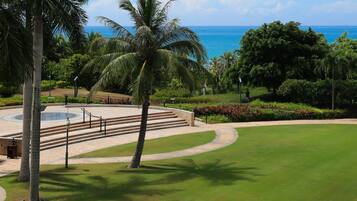 A landscaped area with a circular water feature, palm trees, and a view of the ocean.