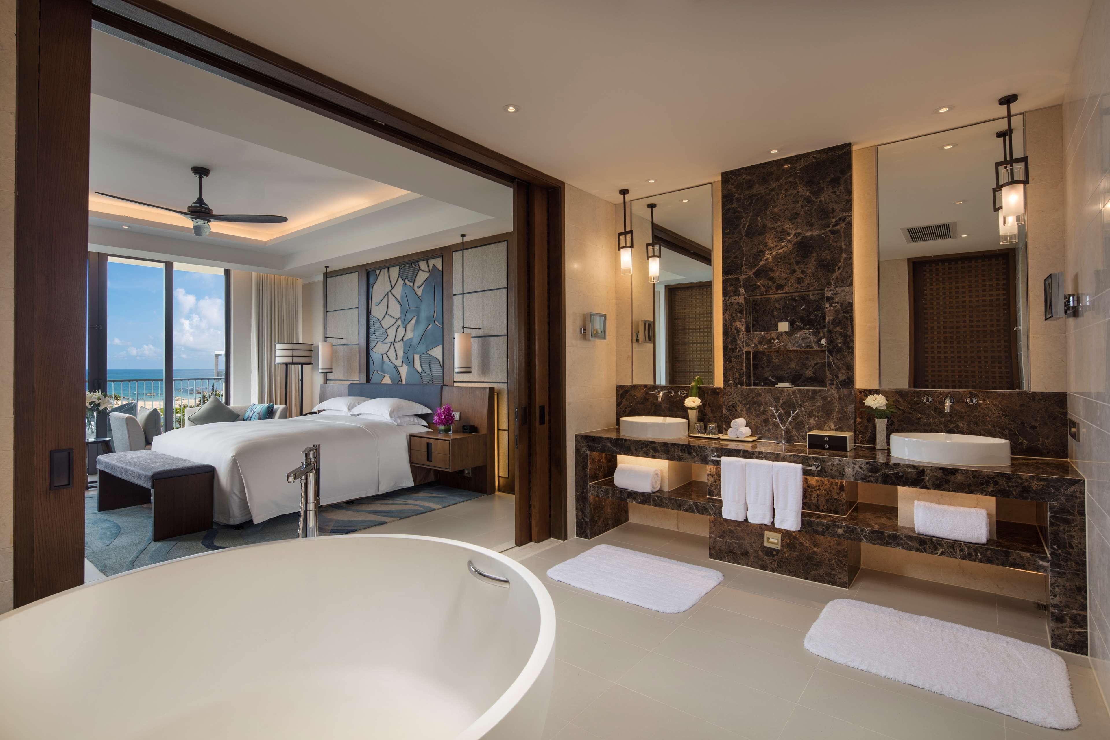 Habitación de hotel moderna con una cama grande, baño independiente con bañera y balcón con vistas al océano.
