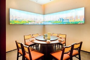 Un salón de conferencias con una mesa redonda, sillas y un cuadro de un paisaje urbano en la pared.