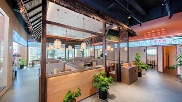 Un espace d’accueil avec un comptoir en bois, des plantes en pot et des luminaires suspendus.