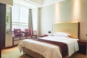 A hotel room with a large bed, a bedside table, a chair, a window with curtains, and a wall-mounted lamp. - Yiaihu Hotel (Huanggang)