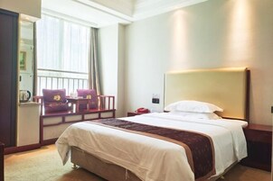 Una habitación de hotel con una cama grande, una mesita de noche, una silla, una ventana con cortinas y una lámpara de pared.