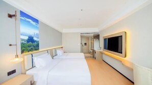 A modern hotel room with two beds, a large window with a cityscape view, a flat-screen TV mounted on the wall, and a bedside table with a lamp. - Yiaihu Hotel (Huanggang)