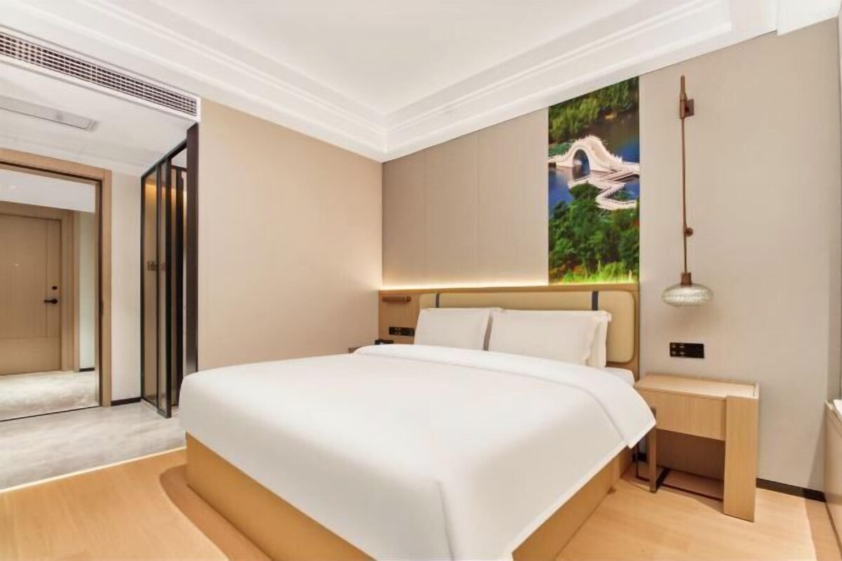 Una habitación de hotel moderna con una cama grande, una mesita de noche, una obra de arte colgada en la pared y una rejilla en el techo.