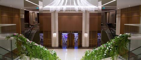 A modern hotel lobby with a central staircase, glass railings, and decorative plants.