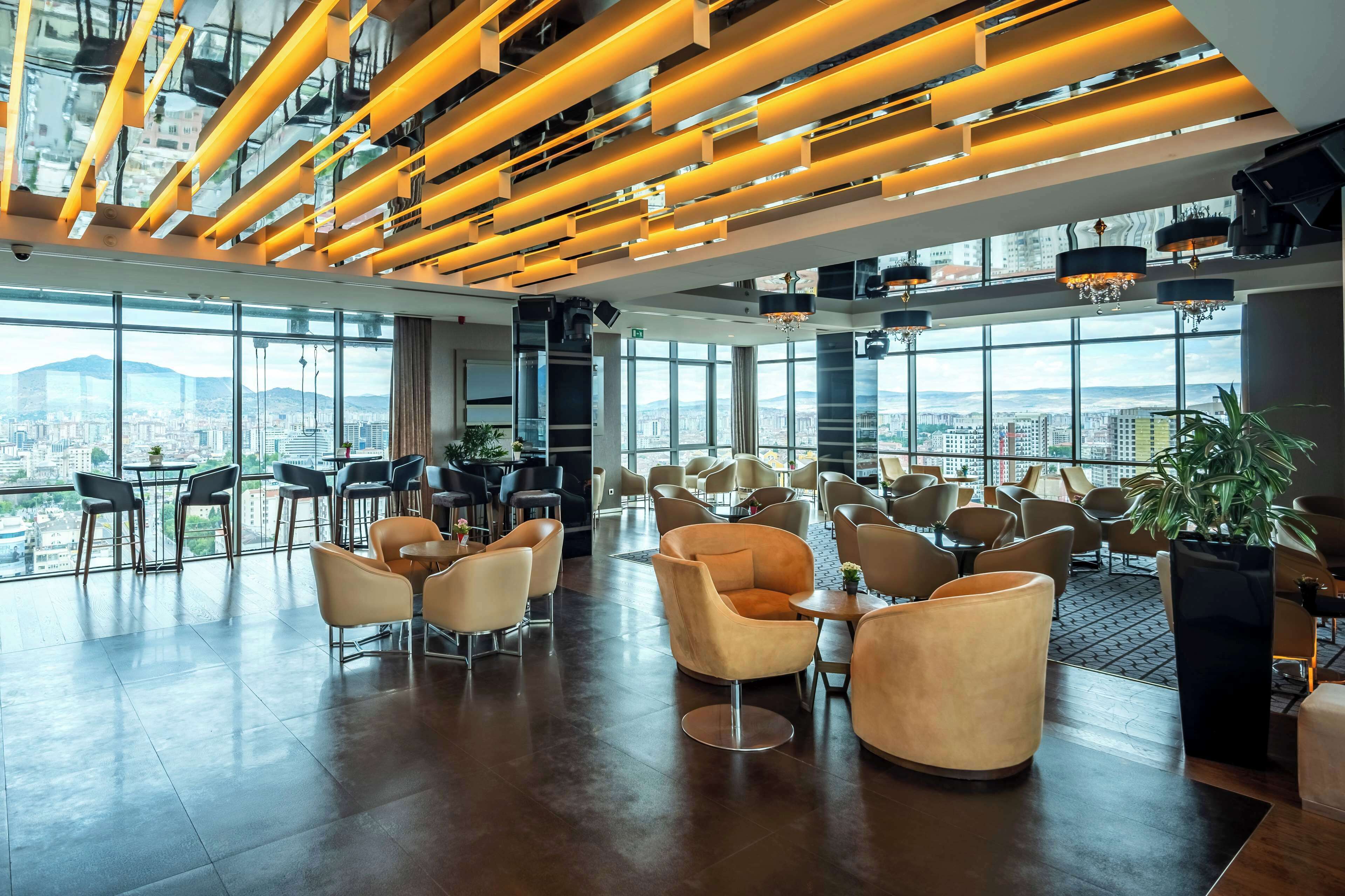 A spacious lobby with modern furniture, large windows offering city views, and a ceiling with linear lighting fixtures.
