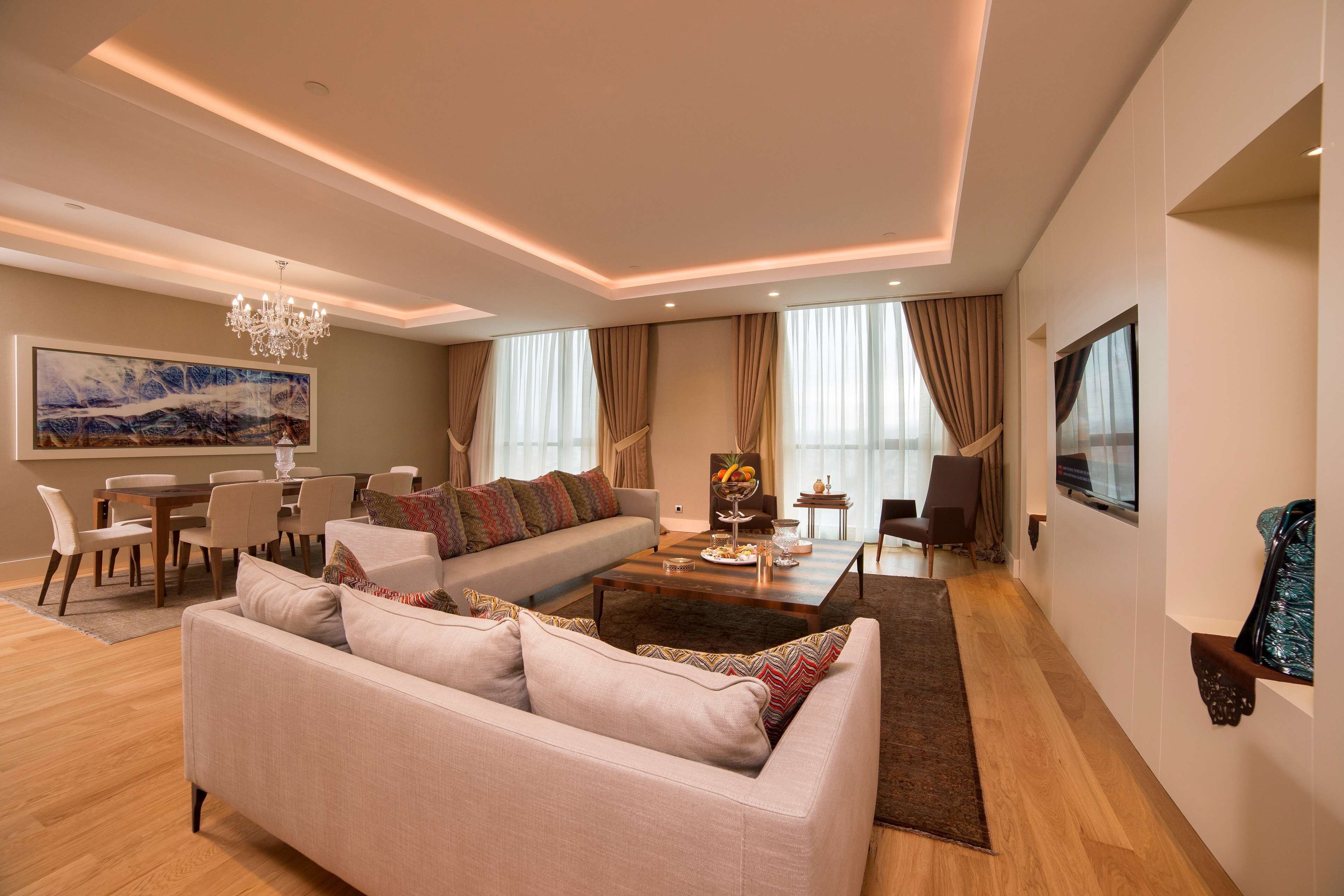 A modern living room with a sofa, dining table, chandelier, and large windows.