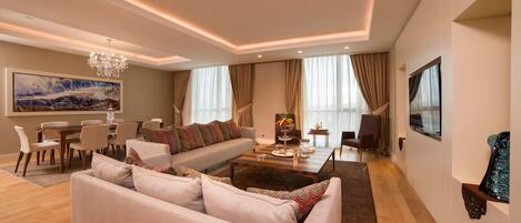 A modern living room with a sofa, dining table, chandelier, and large windows.