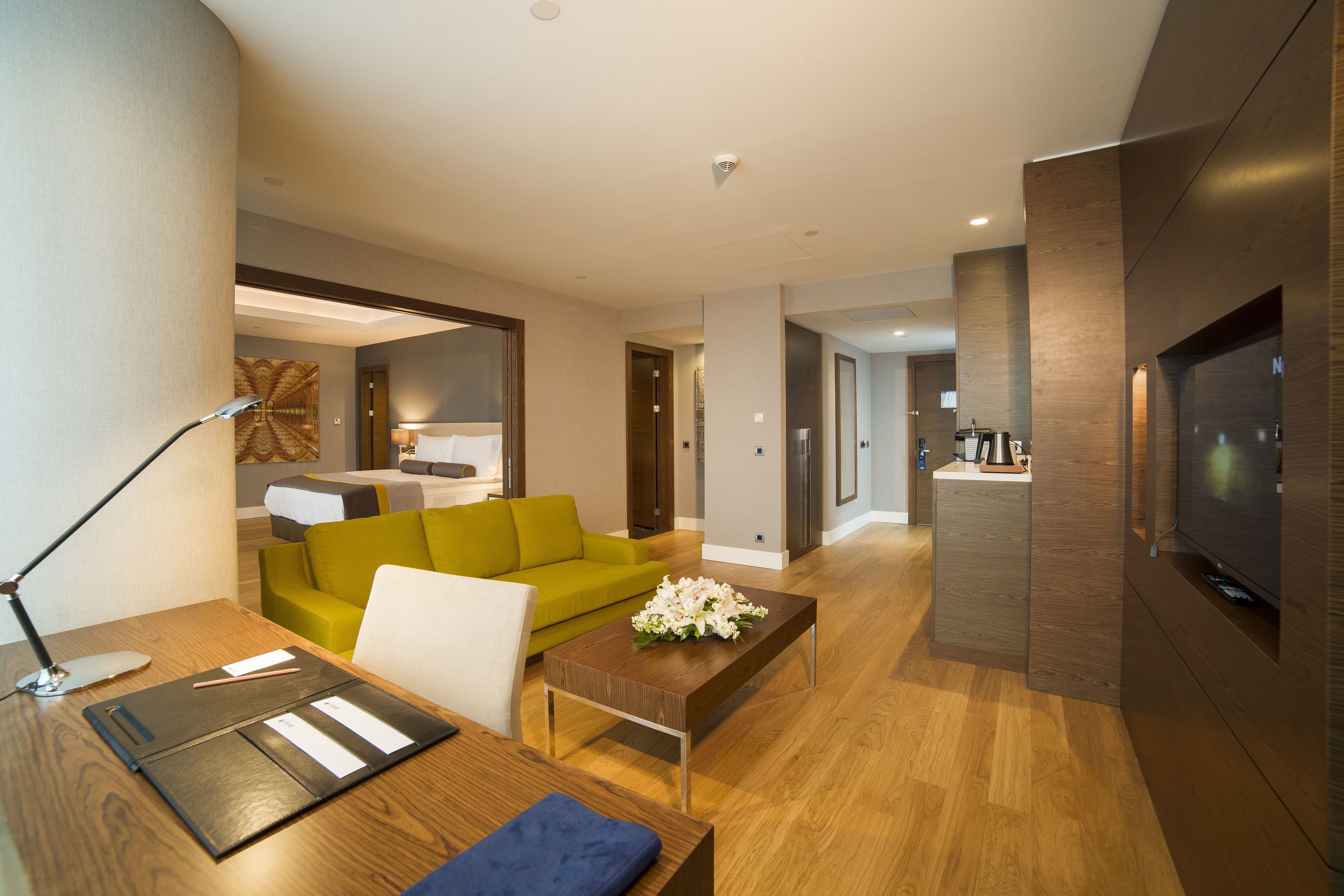 A modern living room with a wooden coffee table, a green sofa, a white armchair, and a flat-screen TV.