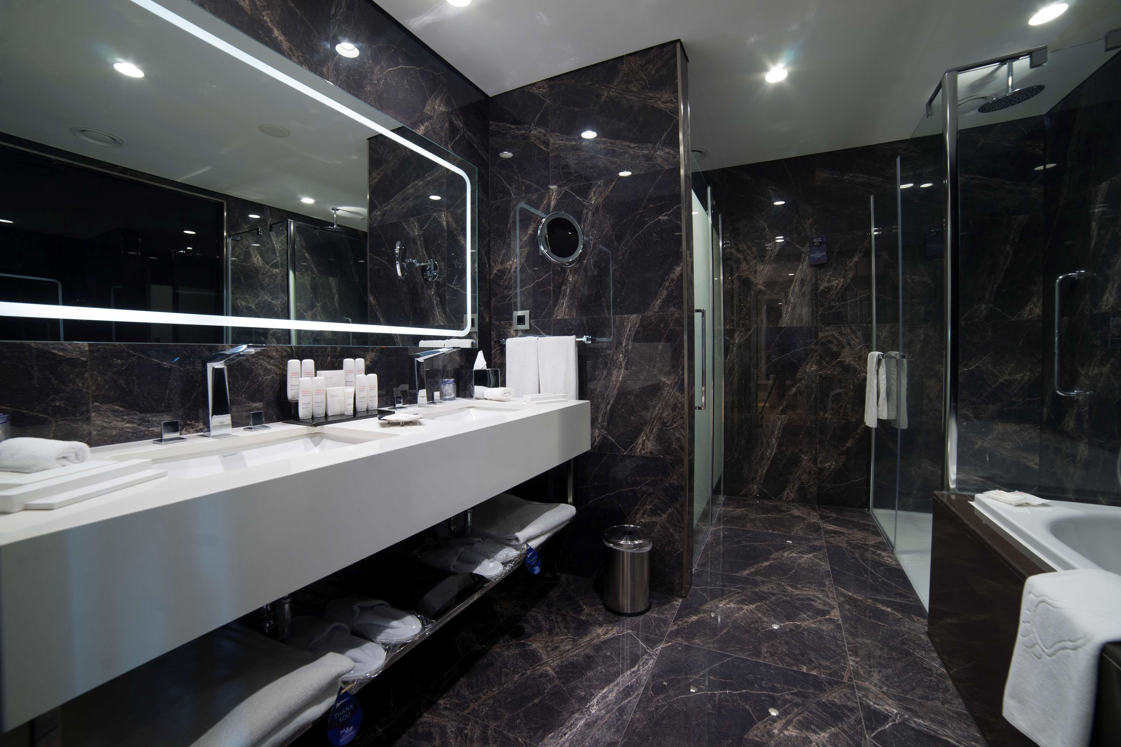 Un baño moderno con un espejo grande, lavamanos blanco y ducha con mampara de vidrio.