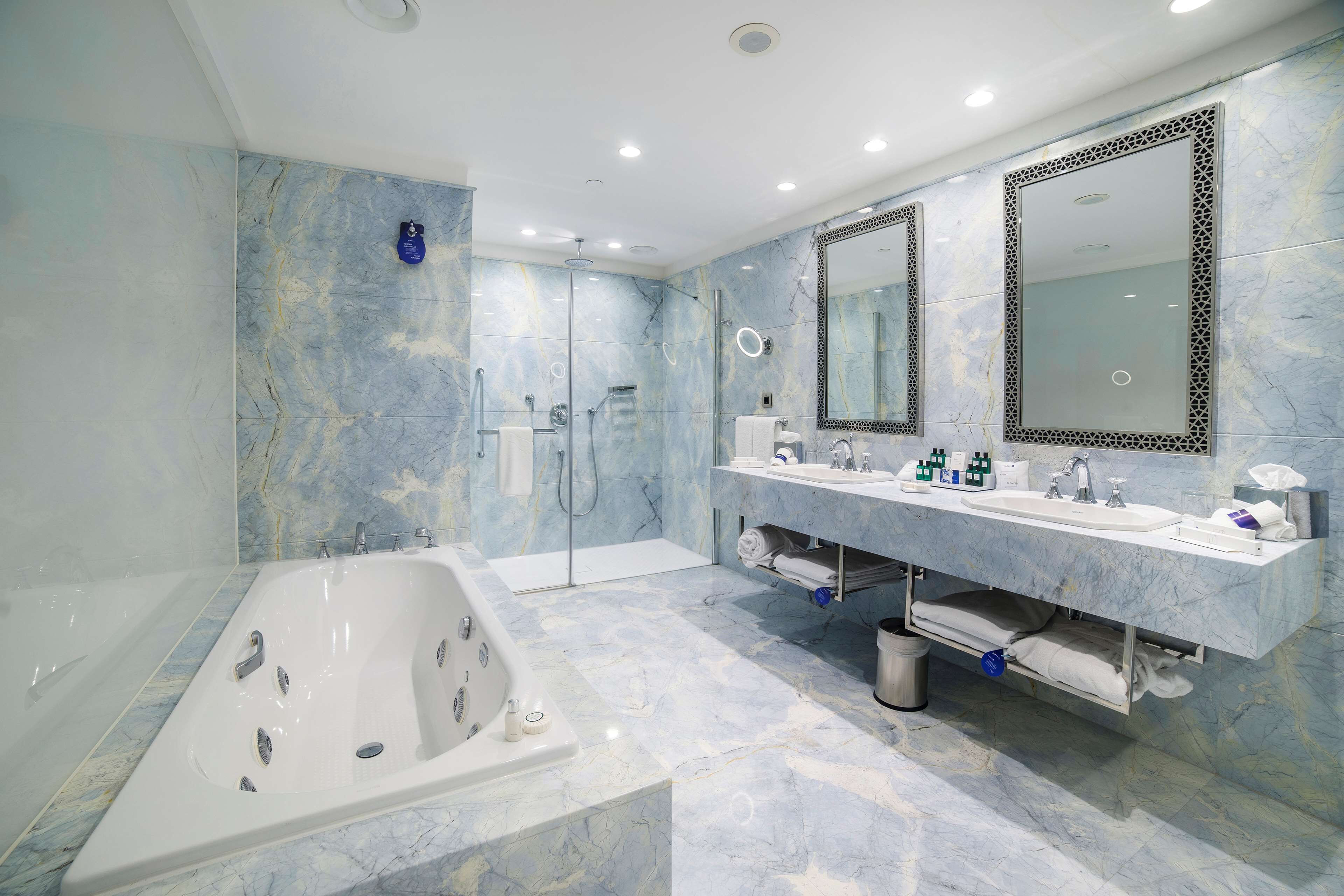 A modern bathroom with a large bathtub, a walk-in shower, and a vanity with two sinks and a large mirror.