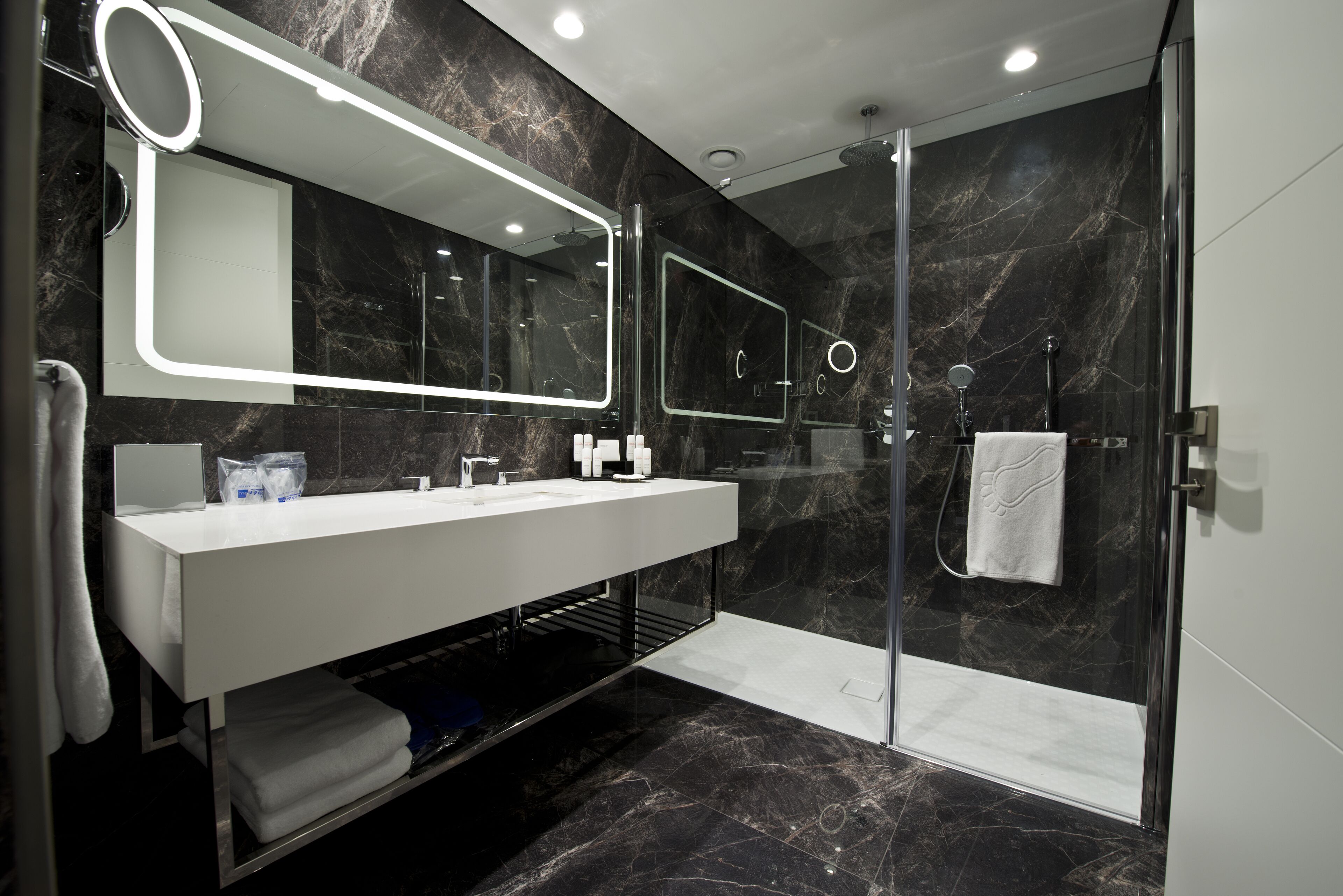 Un baño moderno con ducha envuelta en vidrio, un lavabo blanco con espejo y paredes de mármol.