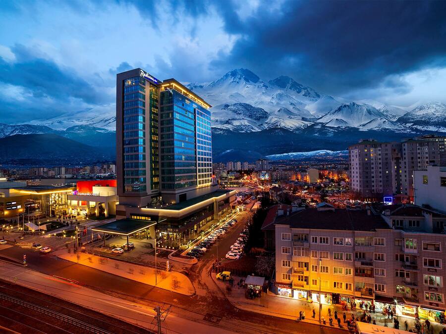Ein Hotel mit modernem Design, einem Parkplatz und Blick auf schneebedeckte Berge im Hintergrund.