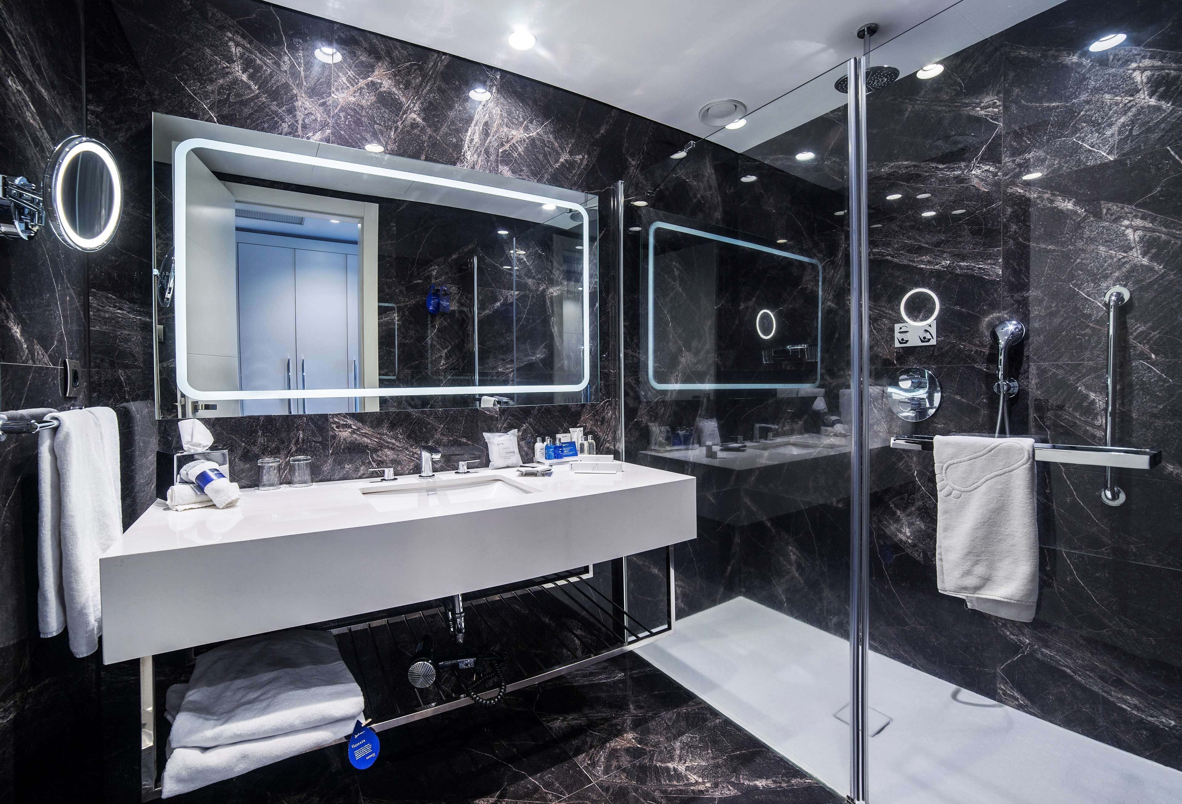 A modern bathroom with a large mirror, a white sink, and a glass-enclosed shower.