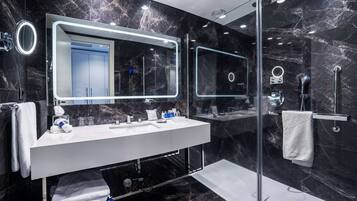 A modern bathroom with a large mirror, a white sink, and a glass-enclosed shower.