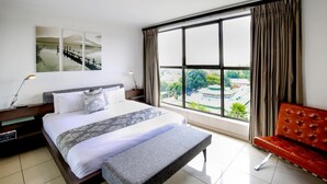 Une chambre d’hôtel avec un grand lit, un banc, une vue sur un parc et un tableau au mur.