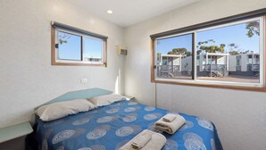 Une chambre à coucher avec un lit, deux fenêtres et une vue sur un ensemble d’immeubles.
